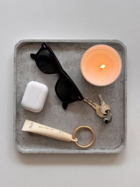 Biyu lip butter, zonnebril en kaars op een betonnen tray